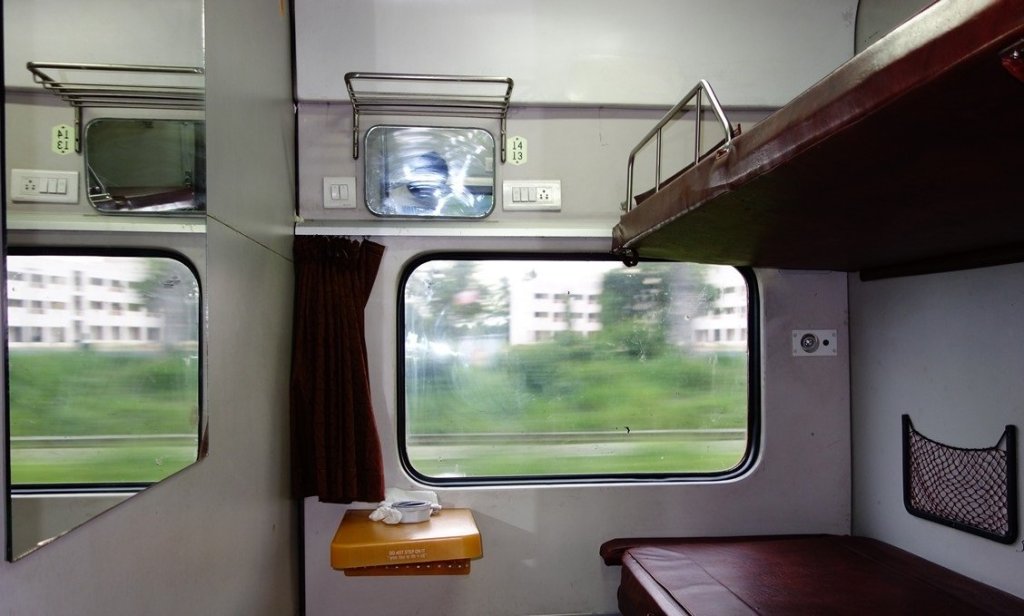 Interior of a train compartment with a window, a top bunk, and a small table.