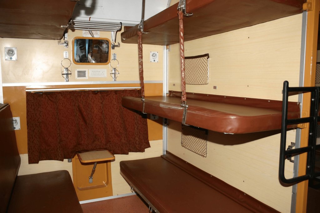 Interior view of a train compartment featuring upper and lower berths with brown leather seating, a window, and a curtain.