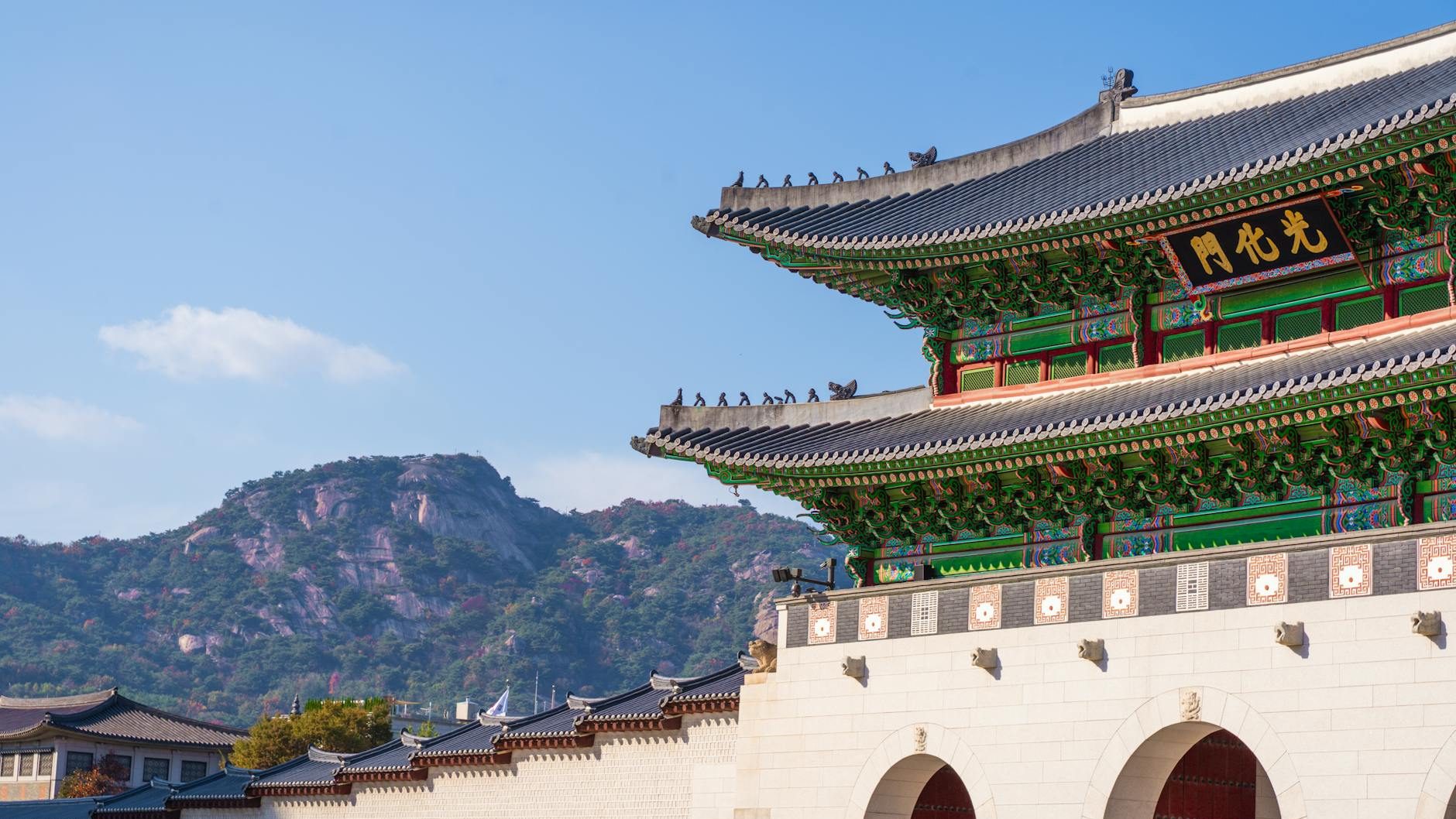 Close-up of a traditional Asian building with ornate roof details and colorful decorations, against a clear blue sky and distant mountain backdrop.