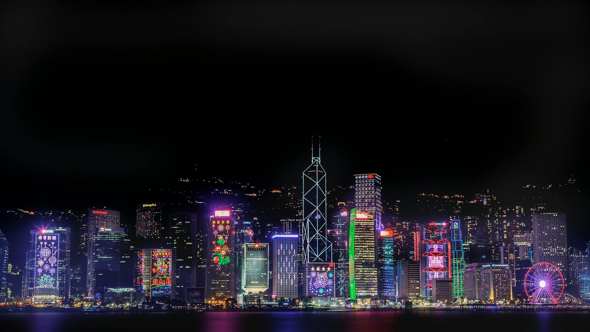 A vibrant skyline of Hong Kong at night featuring illuminated skyscrapers and colorful light displays reflecting on the water.
