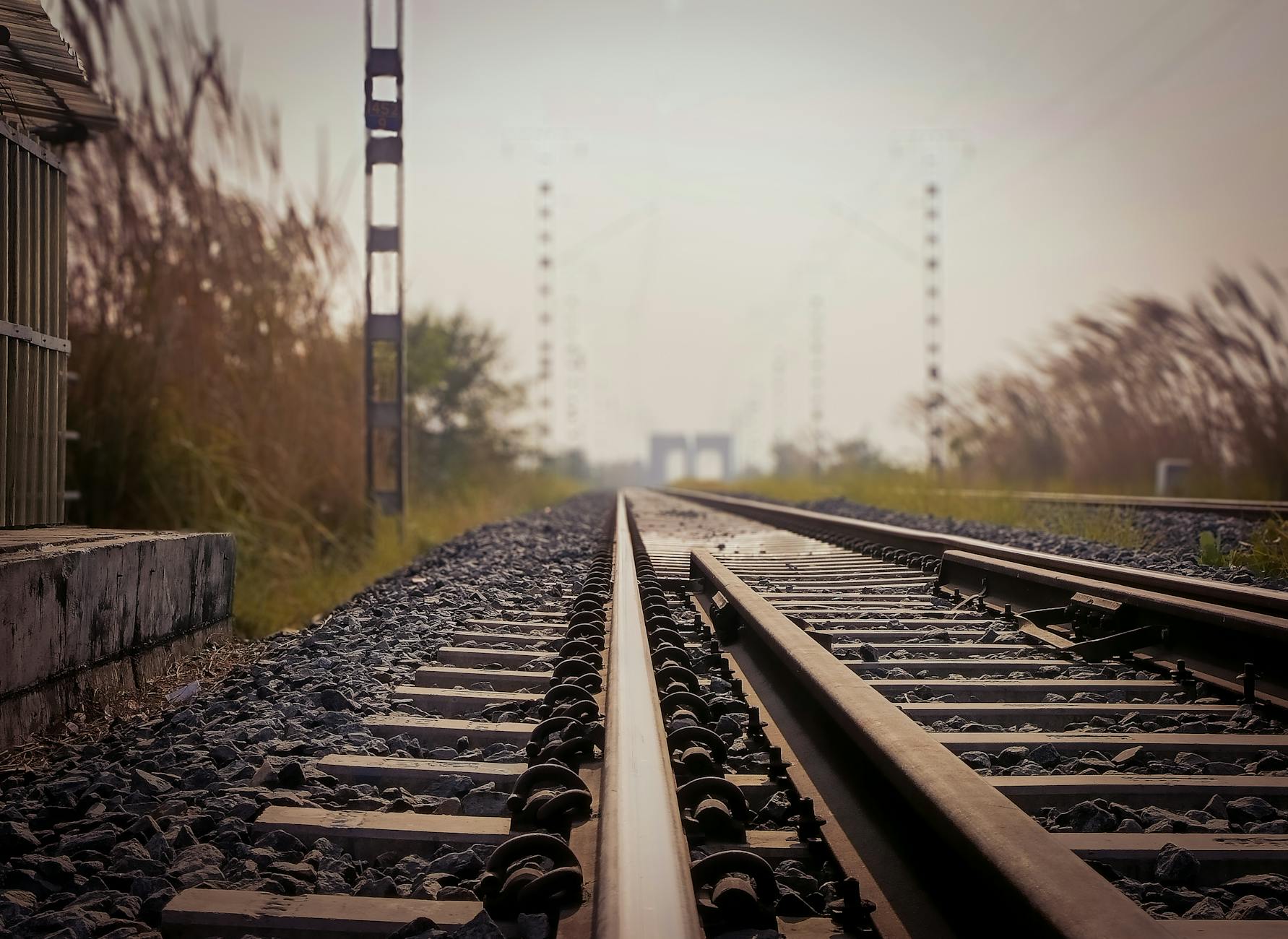 A low-angle view of railway tracks extending into the distance, bordered by grass and signaling poles in the background.