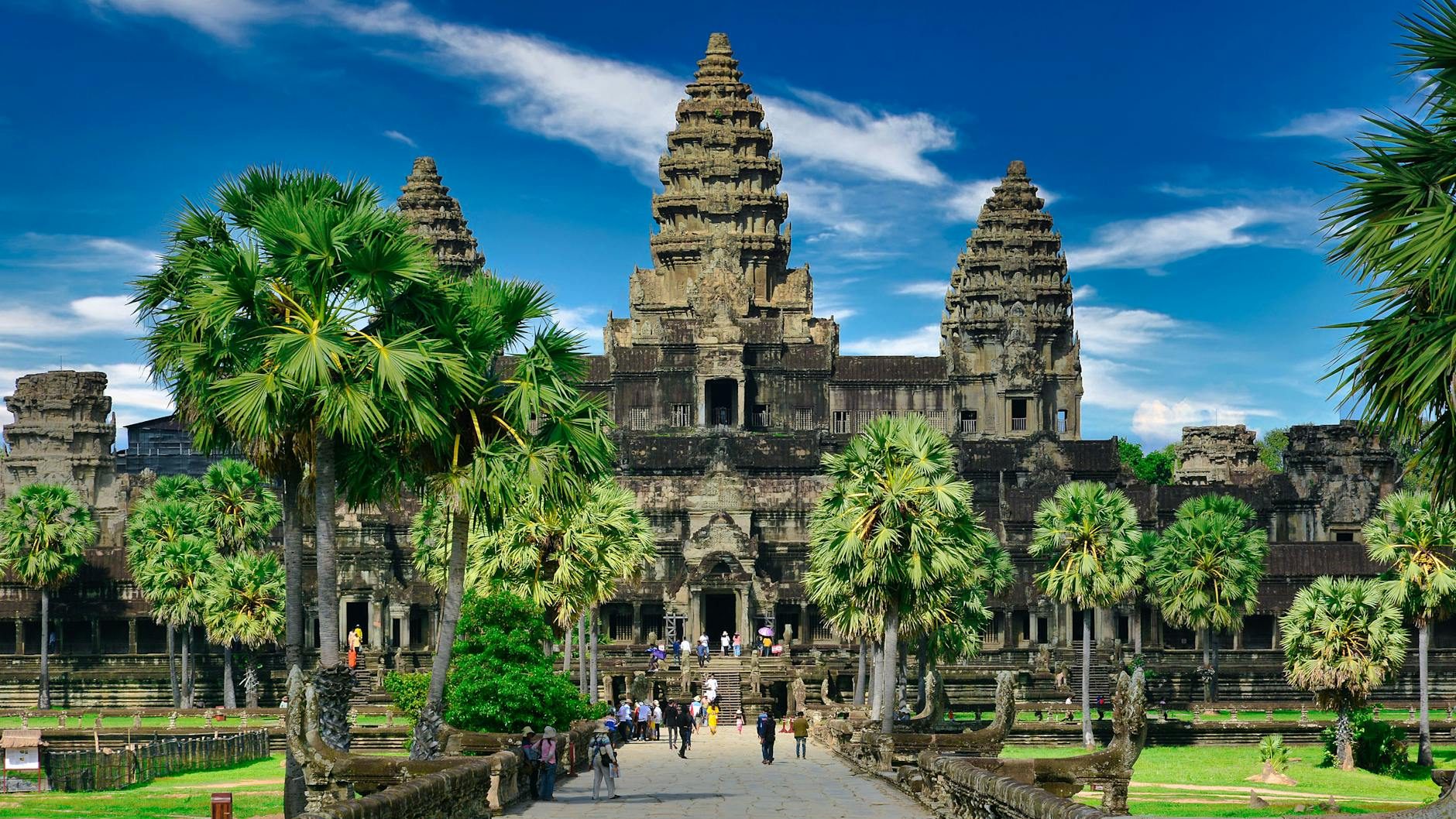 A view of Angkor Wat in Cambodia, featuring intricate temple architecture and palm trees set against a blue sky.