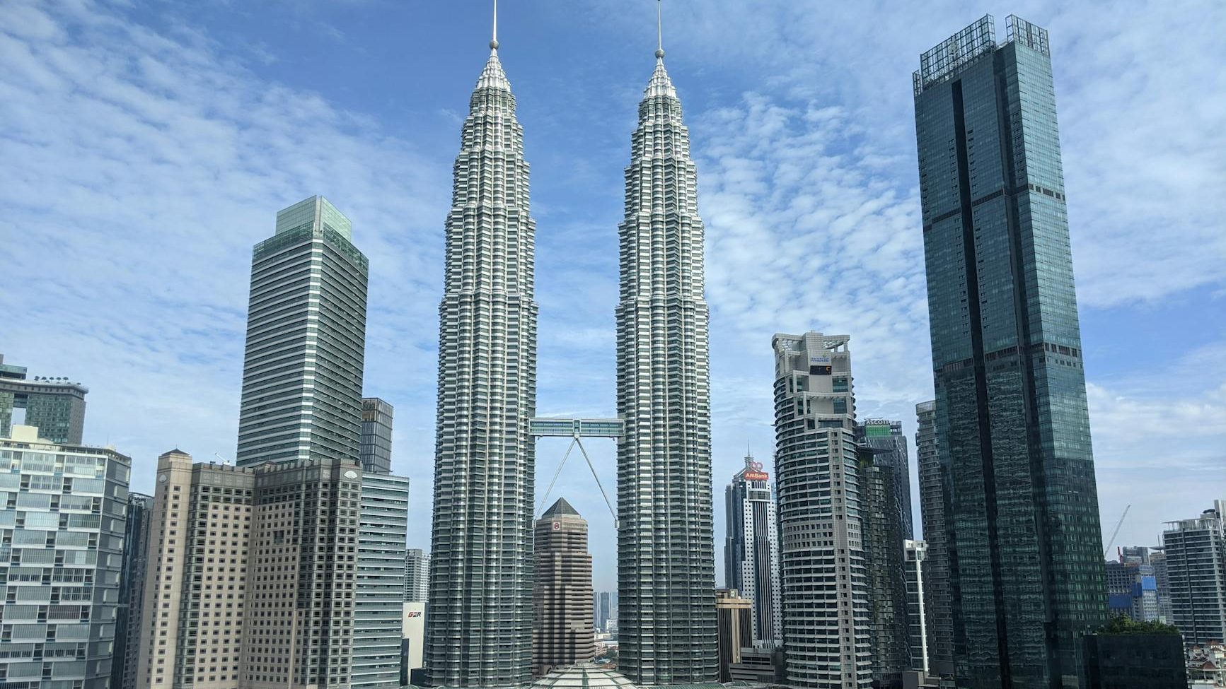 View of the Petronas Towers and surrounding skyscrapers in a cityscape with blue skies.